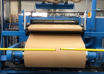 Eine industrielle Papierrolle wird in einer Fabrik durch eine Maschinenvorrichtung gerollt. Die Produktionslinie ist gut sichtbar.