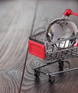 Ein Miniatur-Weltglobus liegt in einem Einkaufswagen auf einem Holztisch, was den internationalen Handel symbolisiert.