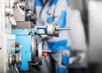 Fokussierte Ansicht eines Arbeiters, der eine Präzisionsbohrmaschine in einer Fabrikumgebung bedient, mit sichtbaren Metallspänen und Kühlflüssigkeit.