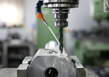 Nahaufnahme eines Arbeiters, der eine CNC-Maschine bedient, wobei Kühlflüssigkeit während des Präzisionsmetallbearbeitungsprozesses versprüht wird.